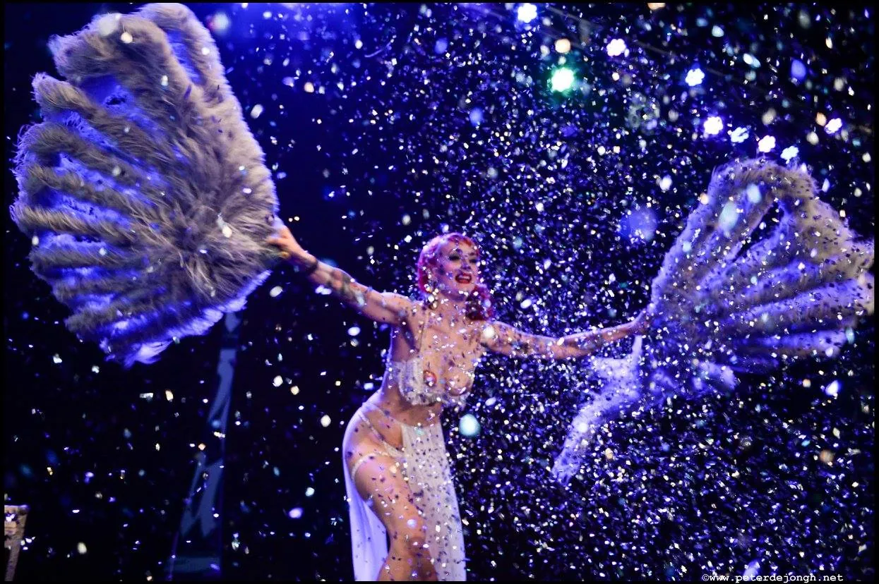 Aerial performer in a lit costume against a dark stage