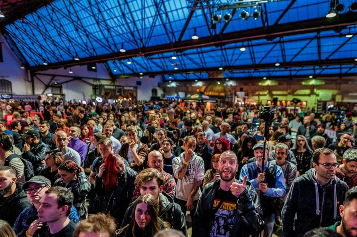 Dense crowd on a convention floor under a steel roof