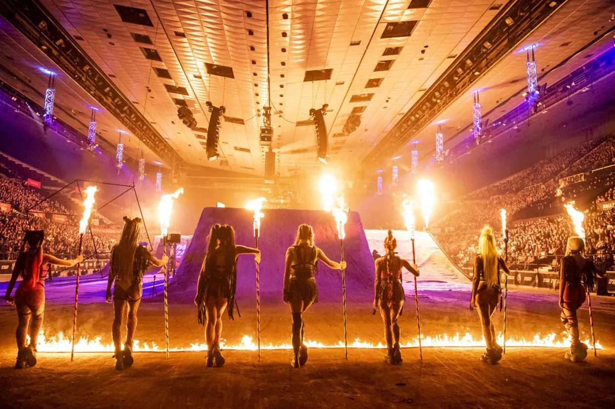 Performers with torches in front of a full arena, flame jets firing